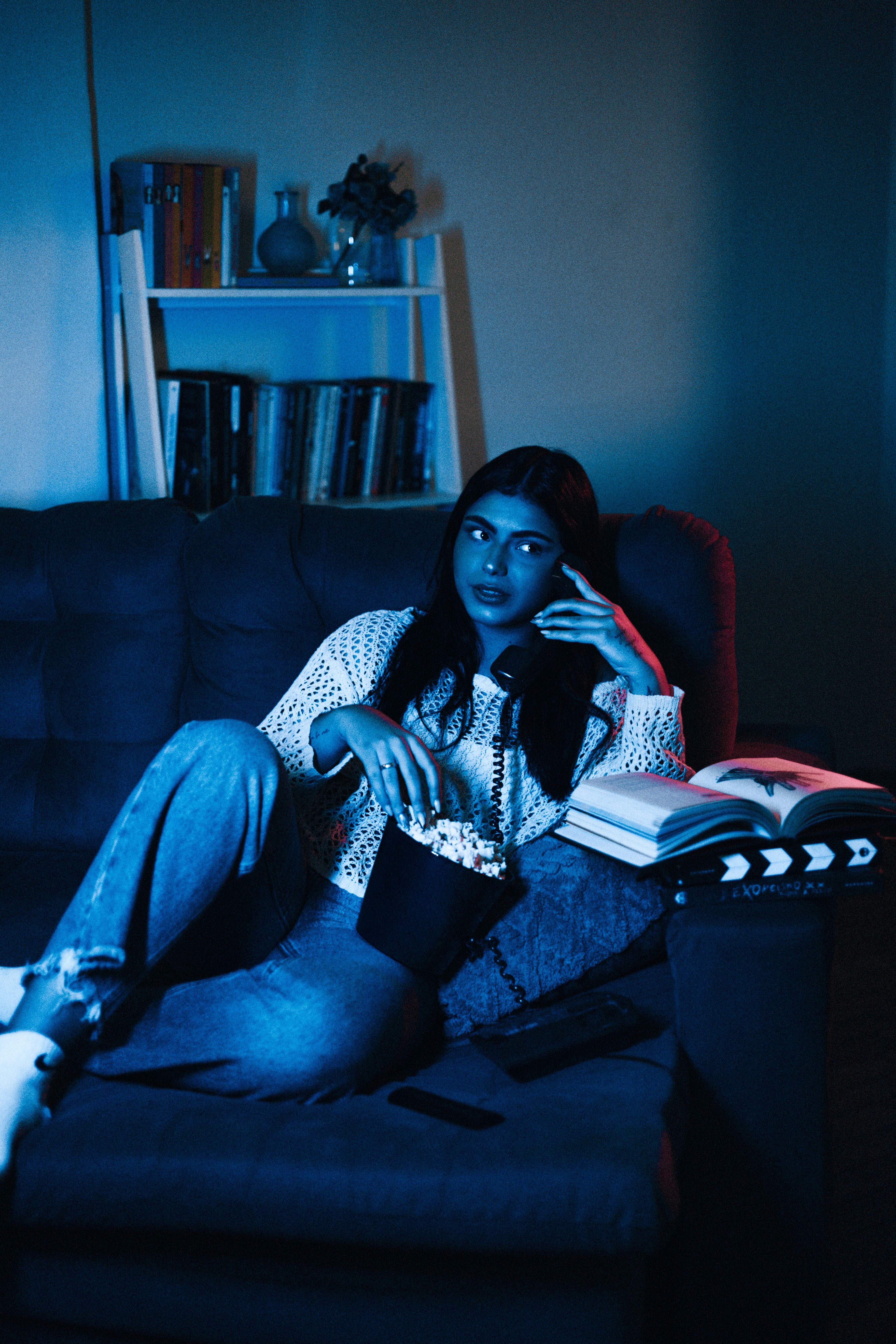 A woman relaxing on a couch with popcorn and a remote control in moody blue movie-night lighting